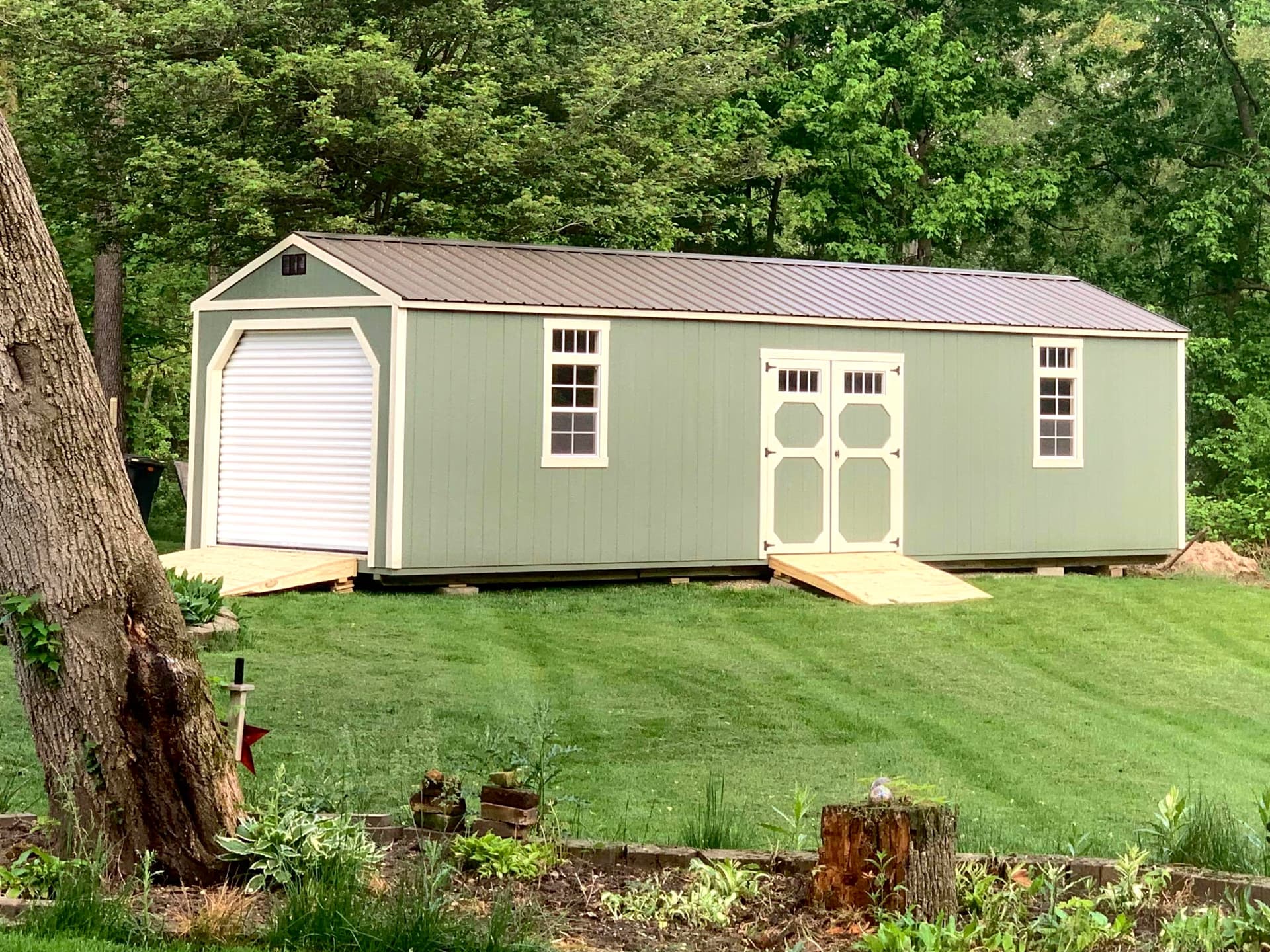 Sage green Amish-built garage surrounded by trees at customer property