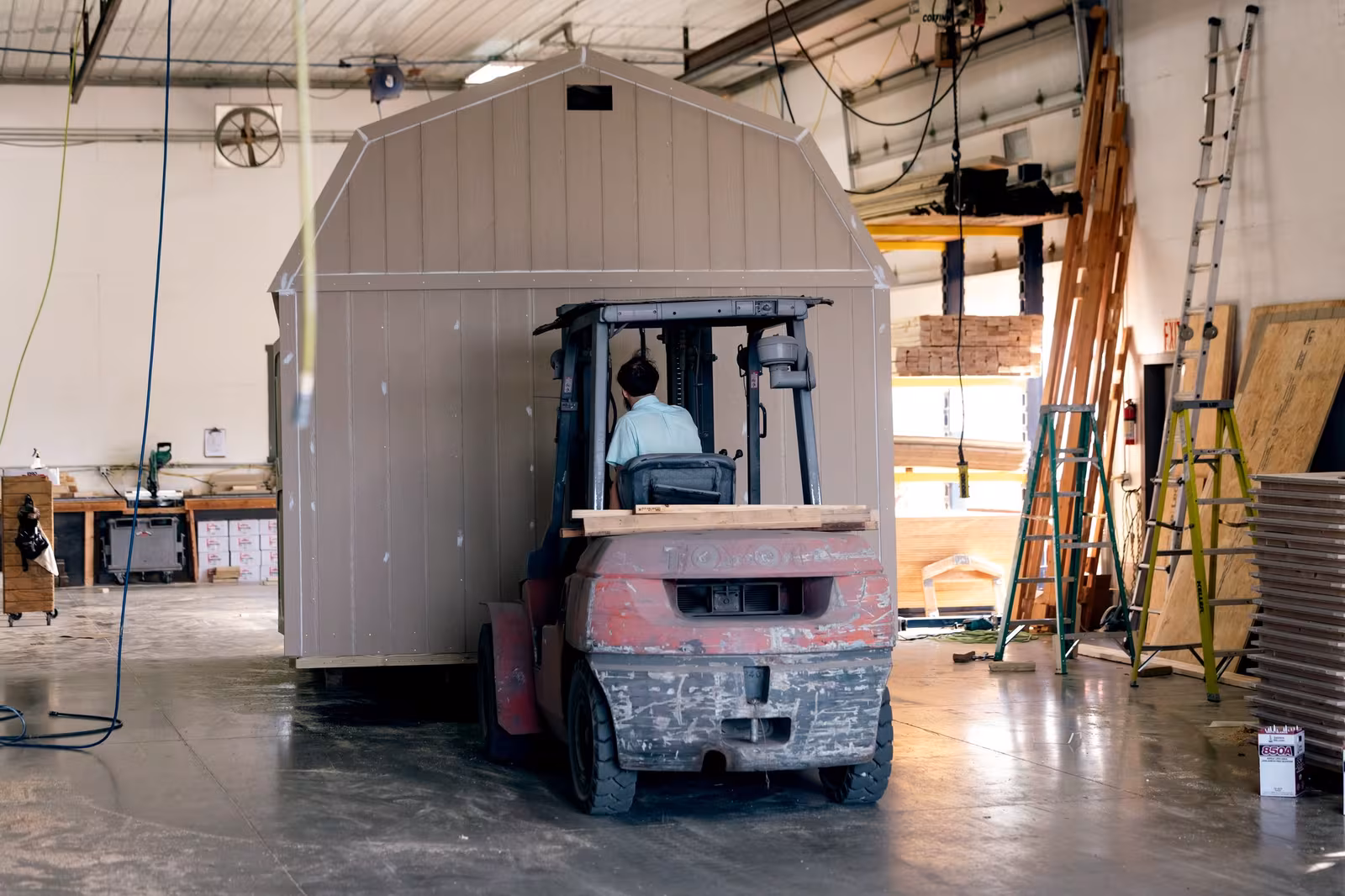A finished Amish-built shed being moved across the workshop by forklift